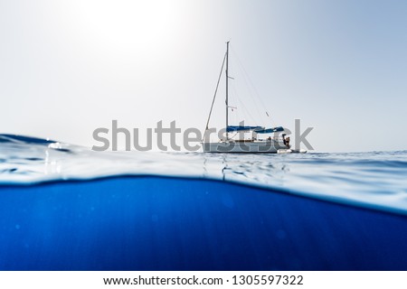 Split shot of the sailing boat in the open sea with clear blue underwater view