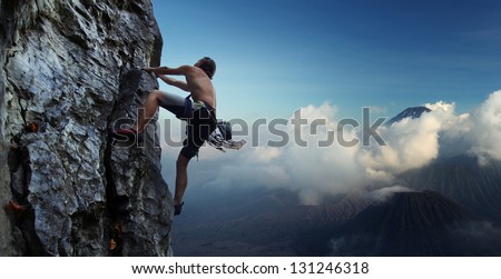 Young man climbing natural rocky wall with volcanoes on the background Young man climbing natural rocky wall with volcanoes on the background