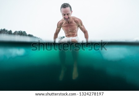 Young man with lean muscular body sits on the ice and going to swim in the cold winter water. Splitted image with underwater view of the ice hole