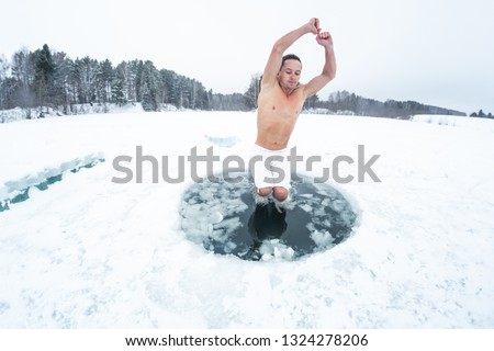 Young man jumps into the ice hole made on the winter lake