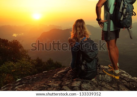 Tourist with backpacks enjoying sunrise on top of a mountain