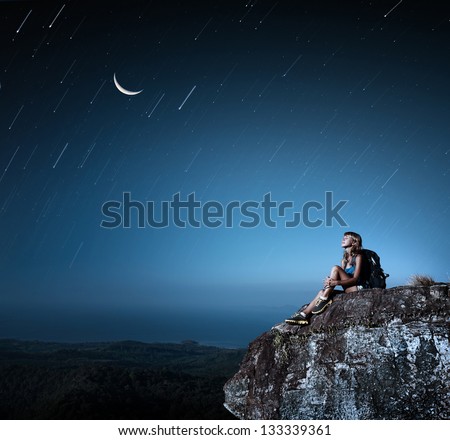Tourist with backpack relaxing on top of a mountain at bright night with stars in a sky Tourist with backpack relaxing on top of a mountain at bright night with stars in a sky