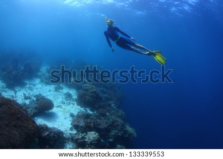 Young lady swimming underwater on a breath hold by a coral reef wall
