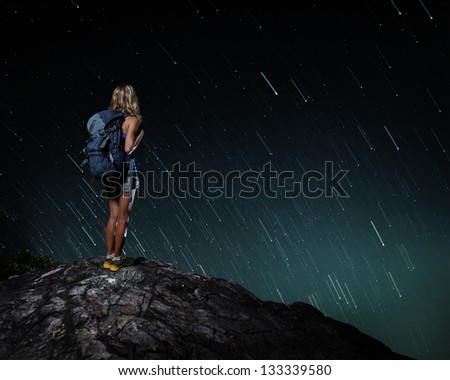 Tourist with backpack standing on top of a mountain and enjoying night sky view with stars