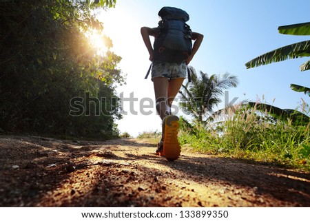 Hiker with backpack walking on rural road with trees on sides