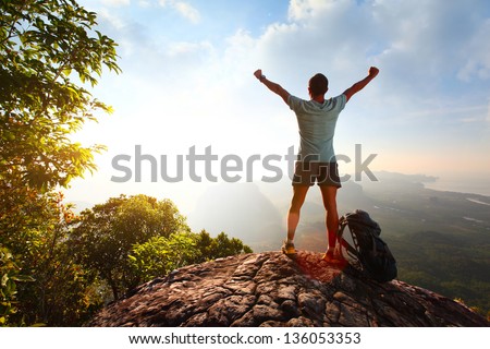 Hiker With Backpack Standing On Top Of A Mountain With Raised Hands