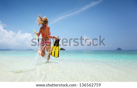 Young lady running into tropical sea with snorkeling equipment at sunny day
