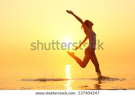 Young lady running and jumping on a beach in shallow sea