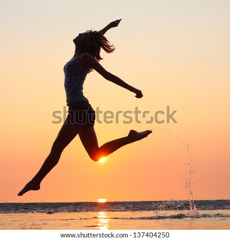 Young lady running and jumping on a beach in shallow sea