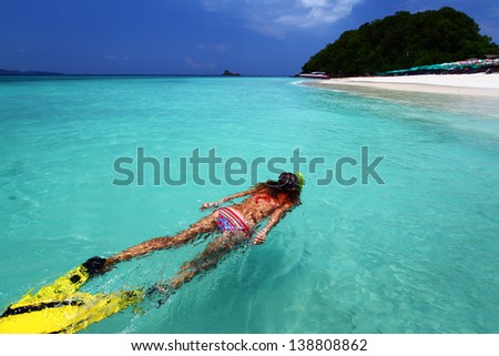 Young lady snorkeling in a turquoise tropical sea by a white sandy beach