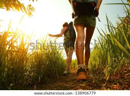 Two young ladies walking with backpacks through green lush meadow