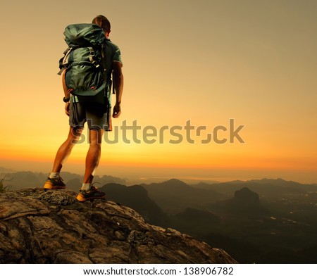 Hiker With Backpack Standing On Top Of A Mountain And Enjoying Sunrise