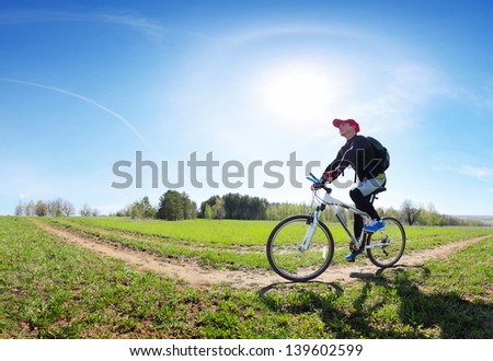 Young man cycling on a rural road through green spring meadow at sunny day