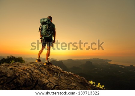 Hiker With Backpack Standing On Top Of A Mountain And Enjoying Sunrise