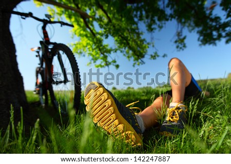 Young lady relaxing on a green meadow after cycling. Focus on a foot