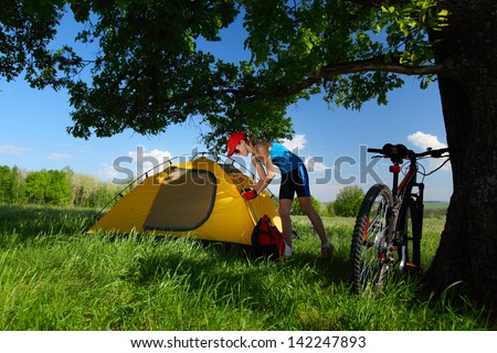 Young sporty lady setting up a tent in a meadow under big oak\'s brunch