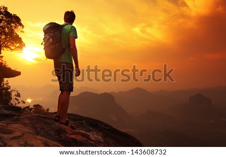 Hiker with backpack standing on top of a mountain and enjoying sunrise