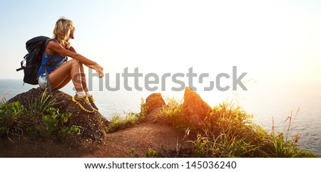 Hiker with backpack relaxing on a rock and enjoying sunset Hiker with backpack relaxing on a rock and enjoying sunset