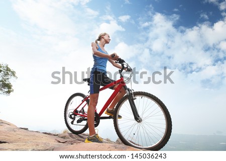 Young sporty lady standing with bicycle on a blue sky background