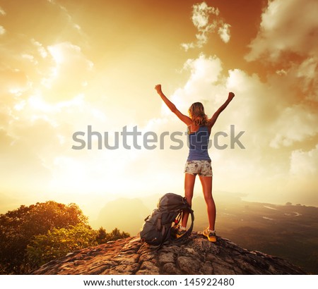 Hiker with backpack enjoying sunrise from top of a mountain