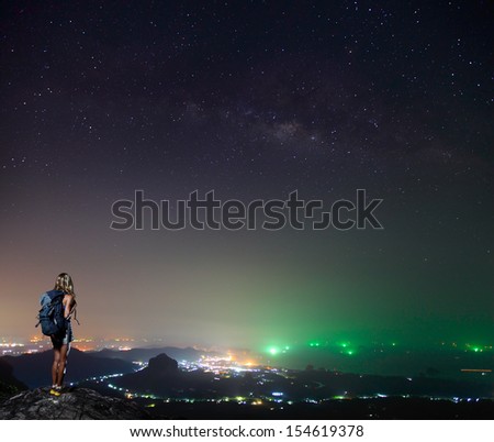 Hiker standing on top of a mountain and enjoying night sky view with a lots of stars and artificial city lights