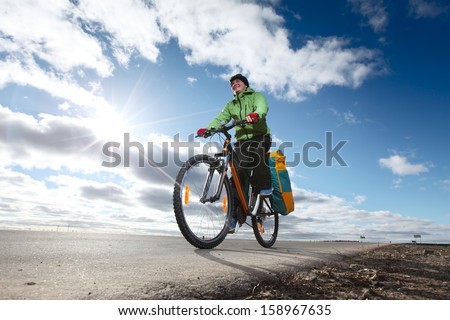 Happy bicycle tourist with loaded bike riding on an empty road