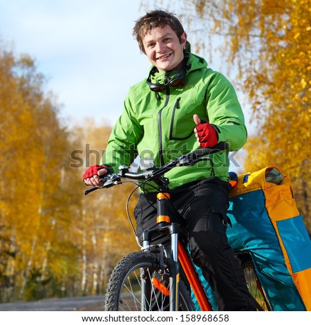 Young happy bicycle tourist with his loaded bike standing on an autumn road in a sunny day