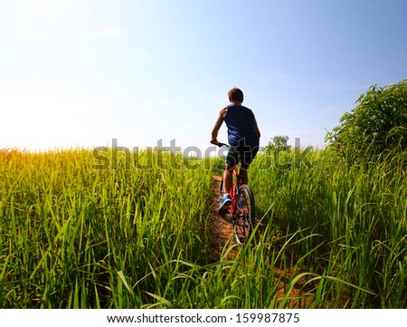 Young rider cycling through a green lush meadow in sunny day