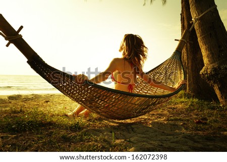 Young lady relaxing in the hammock on the tropical beach and enjoying sea view