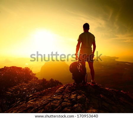 Hiker standing with backpack on top of a mountain and enjoying sunrise