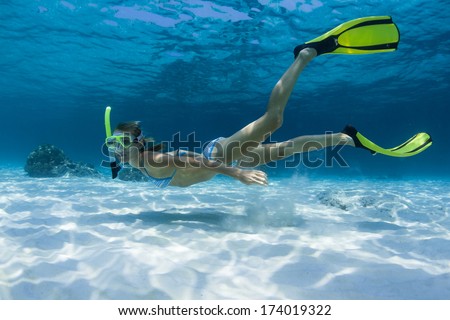 Young lady swimming underwater on a breath hold in a tropical sea with yellow fins