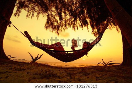 Young lady reading the book in the hammock on tropical beach at sunset