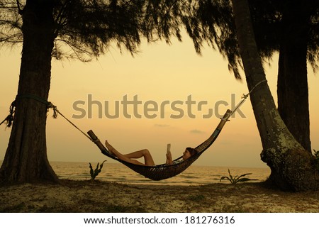 Young lady reading the book in the hammock on tropical beach at sunset