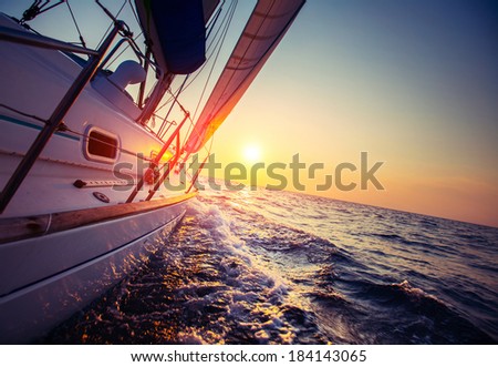 Sail boat with set up sails gliding in open sea at sunset