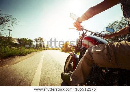 Biker riding motorcycle on an empty road at sunny day