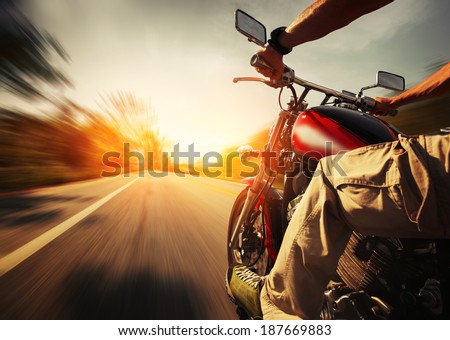 Biker riding motorcycle  on an empty road at sunny day