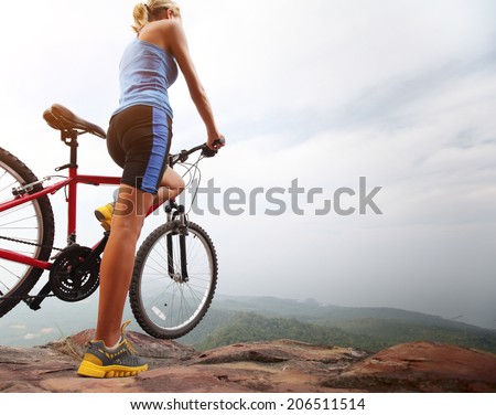 Young sporty lady standing with bicycle on top of a mountain