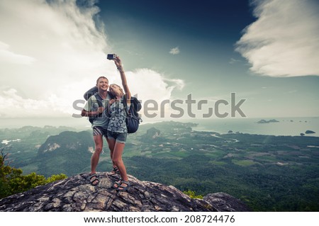 Couple of hikers taking photo of themselves on top of the mountain with green valley on the background