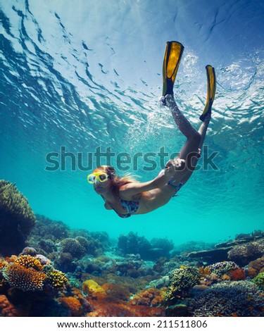 Underwater shot of the young lady gliding over vivid coral reef on a breath hold