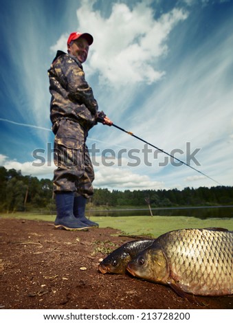 Mature fisherman smiling and looking to his fish (Cyprinus carpio) on the ground. Focus on the fish