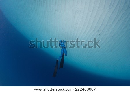 Underwater shot of the free diver in blue suit over sandy sea bottom
