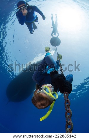 Lady free diver descending along the metal chain using his hands (free immersion). Safety buddy descending close to the athlete