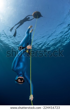 Lady free diver descending along the rope linked to the buoy on surface. Free immersion discipline