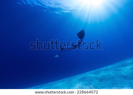 Lady free diver swimming over sandy bottom with mono fin
