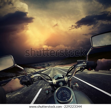 Rider on the motorcycle moving towards dark storm clouds on the asphalt road