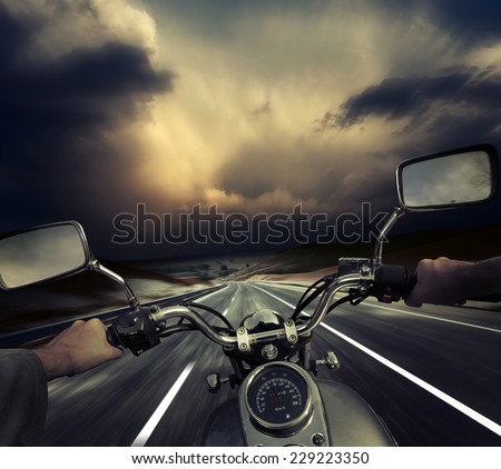 Rider on the motorcycle moving towards dark storm clouds. Road and sky are motion blurred