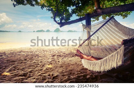 Young lady relaxing in the hammock on the sandy beach with view on remote tropical islands