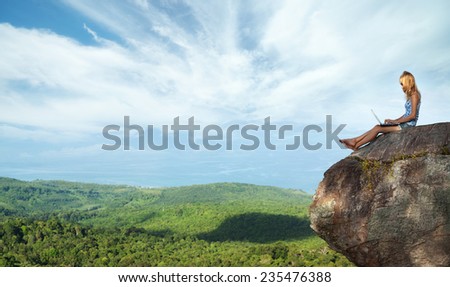 Young lady sitting on top of the mountain with laptop