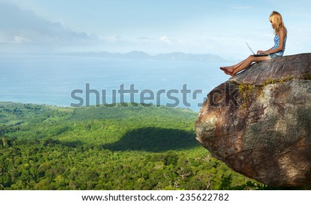 Young lady sitting on top of the mountain with laptop