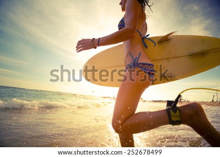 Young lady running into the sea with surf board at sunset